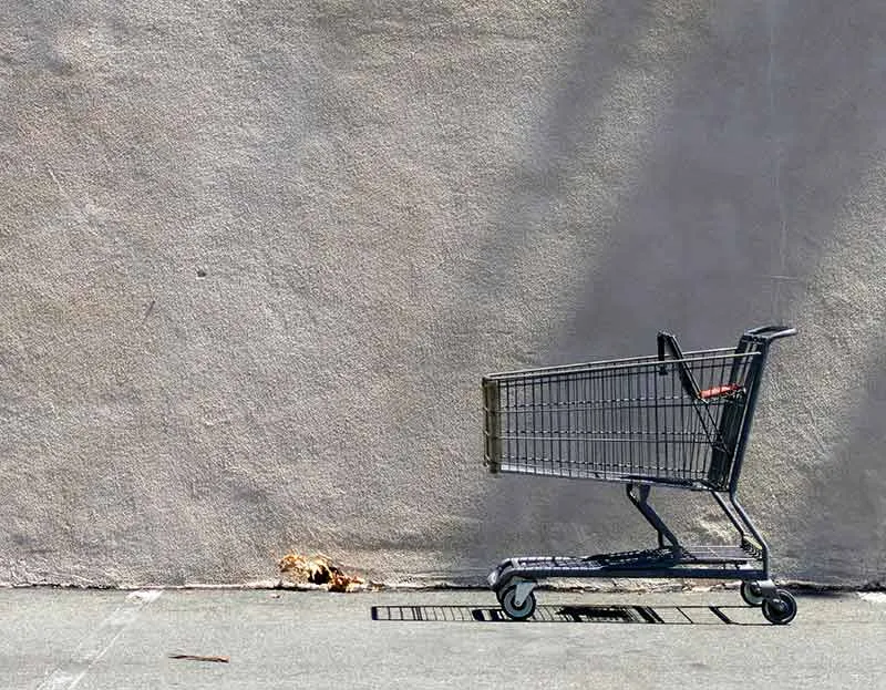 Empty shopping cart against a blank grey wall