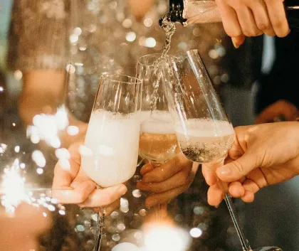 Champagne being poured into three glasses held by people at a celebration