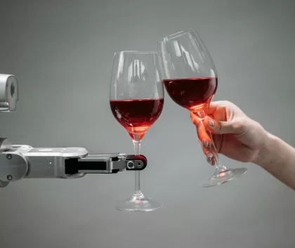 Human hand holding a wine glass and cheersing a robot holding a wine glass 